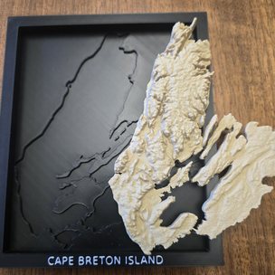 The same print in two pieces: the empty black plate with the coastline cut into it as a recess, and the cream terrain lifted out beside it.